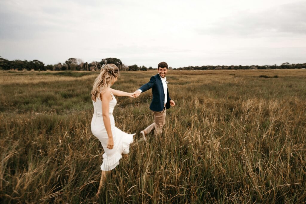 Home Happy couple holding hands and walking through a grassy field, embracing love and freedom.