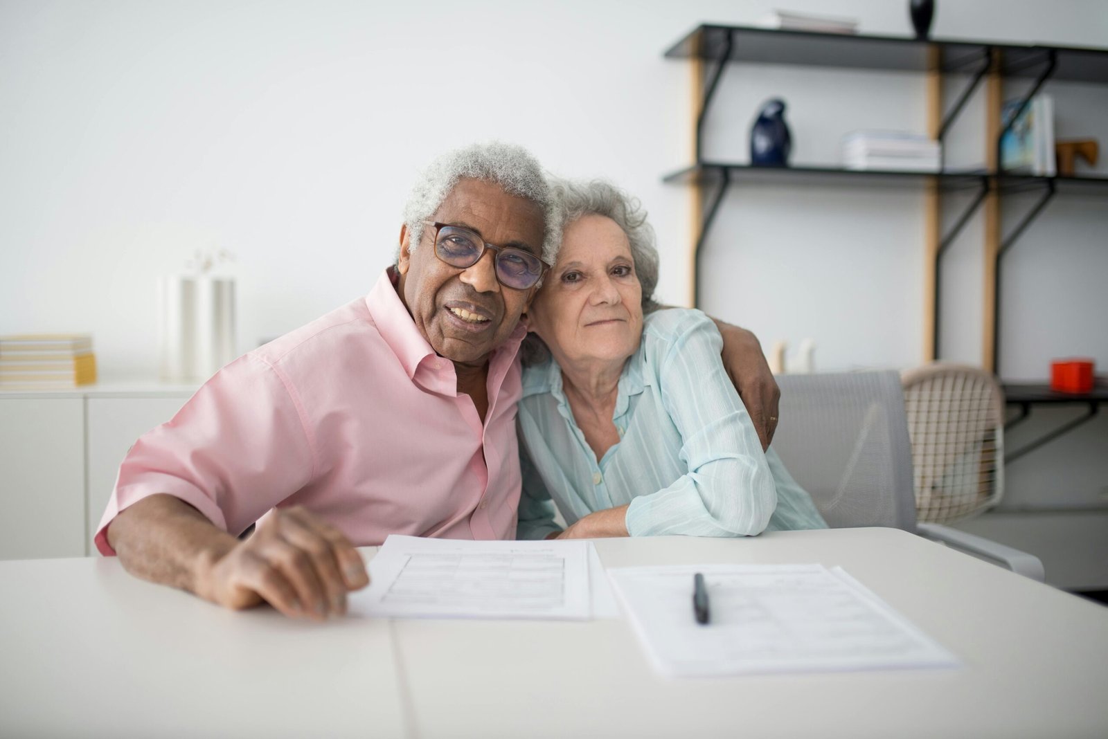 Home Elderly couple smiling and hugging while looking at documents on table indoors.